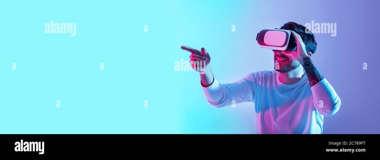 Bekanntschaft mit der virtuellen Welt. Lächelnder Kerl mit Brille zeigt Finger in Neon Stockfoto