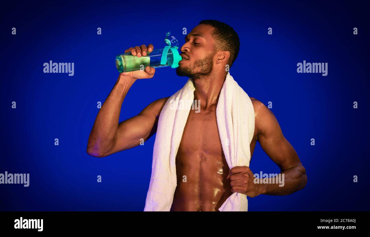 African Fit Mann Trinkwasser Auf Blue Studio Hintergrund Stehen Stockfoto