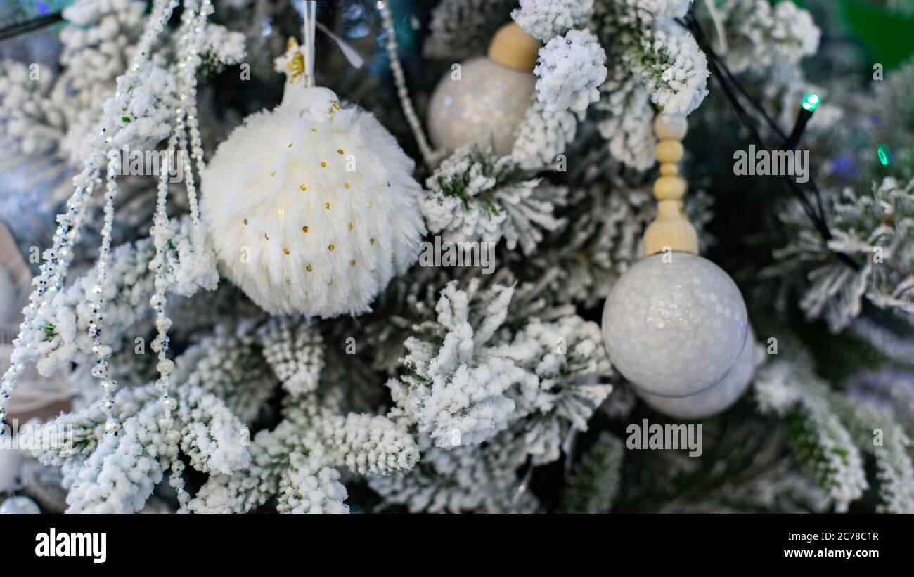 Flauschige weiße Pelzkugel auf einem Weihnachtsbaum mit Kunstschnee. Hintergrund der Neujahrskarte. Weiße pelzige Weihnachtsbaumschmuck Stockfoto