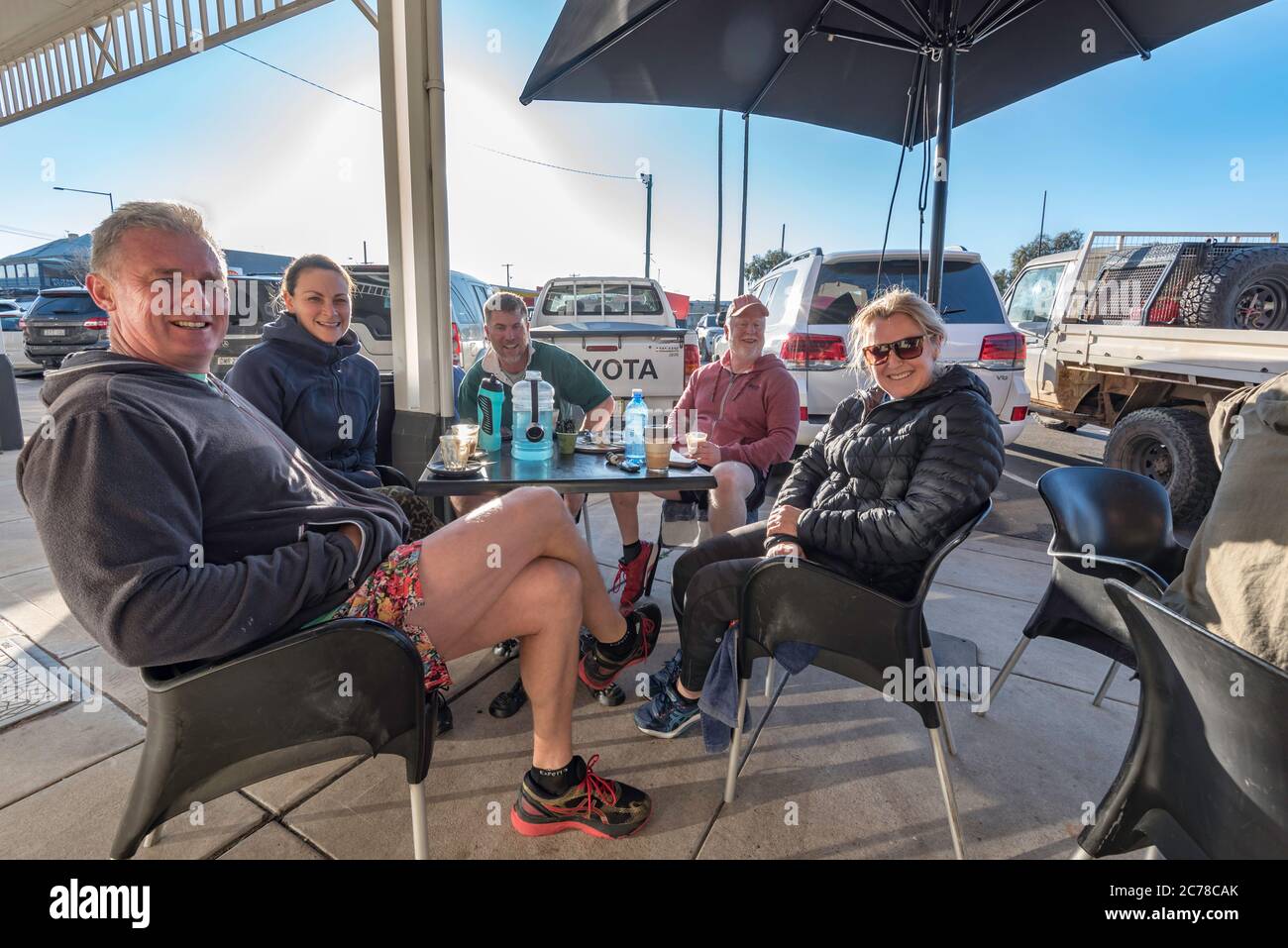 Eine Gruppe von Menschen sitzt lächelnd an einem Wintermorgen an einem Tisch im Freien in der Nähe eines Cafés in Mudgee, New South Wales, Australien Stockfoto