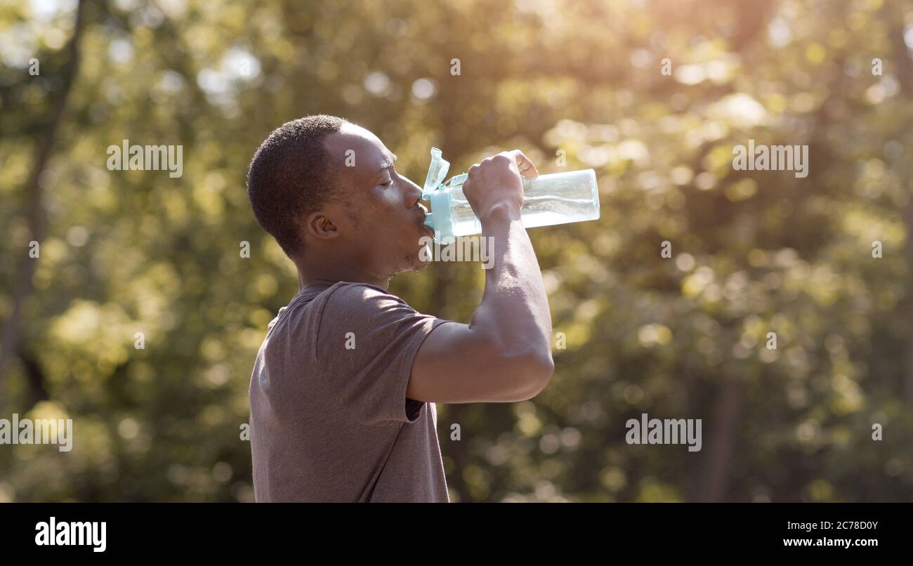 Überhitzter schwarzer Kerl, der Wasser aus der Flasche im Park trinkt Stockfoto