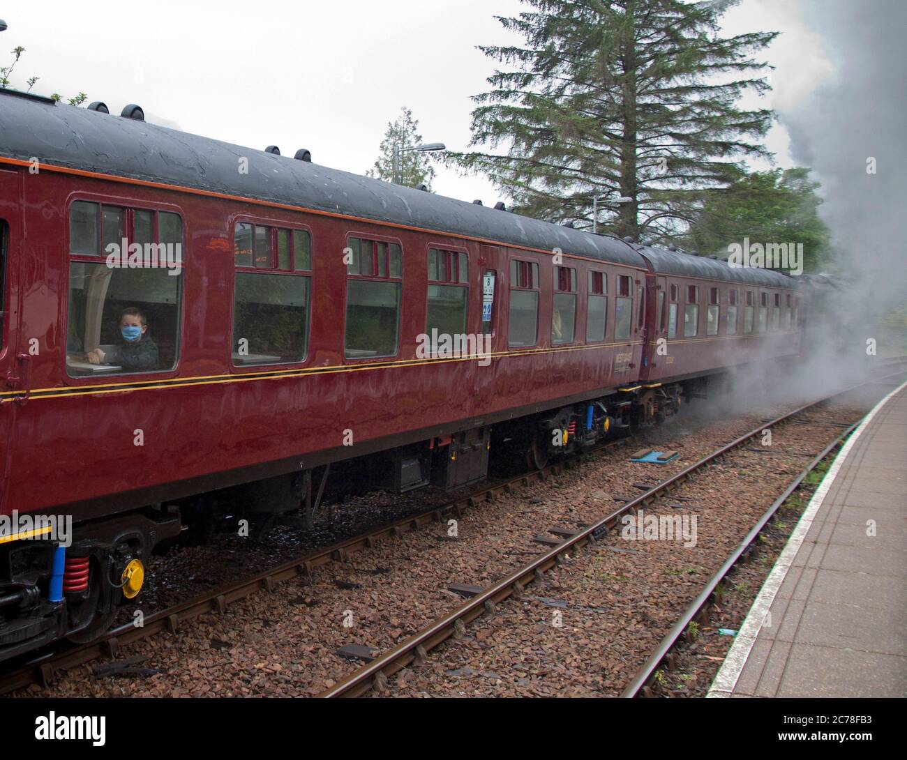 Jacobite Steam Train, Lochaber, Schottland, Großbritannien. Glenfinnan Station, 15. Juli 2020. Der verzögerte Service des Jacobite Steam Train wegen der Covid-19 Coronavirus Lockdown läuft zum ersten Mal im Jahr 2020. Diese 84 Meilen lange Rundreise führt an einer Liste beeindruckender landschaftlicher und historischer Aussichten vorbei. Im Bild: Dampfzug beim Betreten des Glenfinnan Bahnhofs und Passagiere mit Gesichtsbezügen. Der Dienst würde normalerweise seinen Osterdienst um den 30. März beginnen, aber wegen der Pandemie musste er verschoben werden, bis die schottische Regierung entschied, dass es sicher war, in Phase 3 zu gehen. Stockfoto