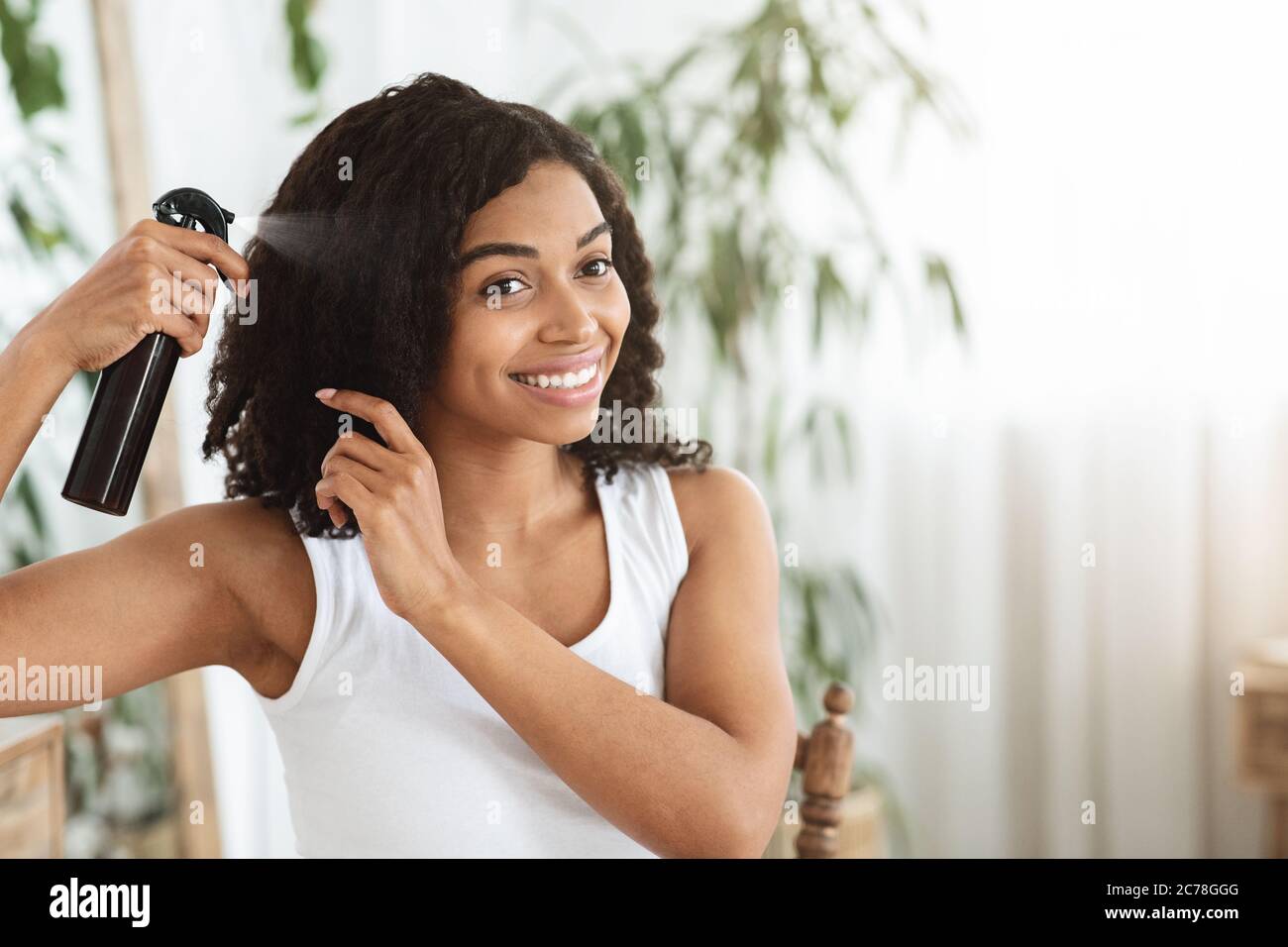 Frisur. Lächelnde Schwarze Frau Anwendung Texturising Spray Auf Ihre Schöne Lockenhaar Stockfoto