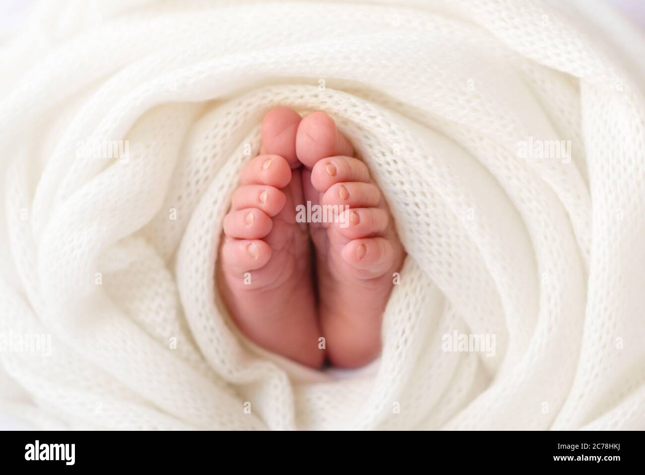 Die Füße des Neugeborenen sind in eine weiße, weiche Hülle gehüllt. Die ersten Tage des Lebens eines Kindes Stockfoto