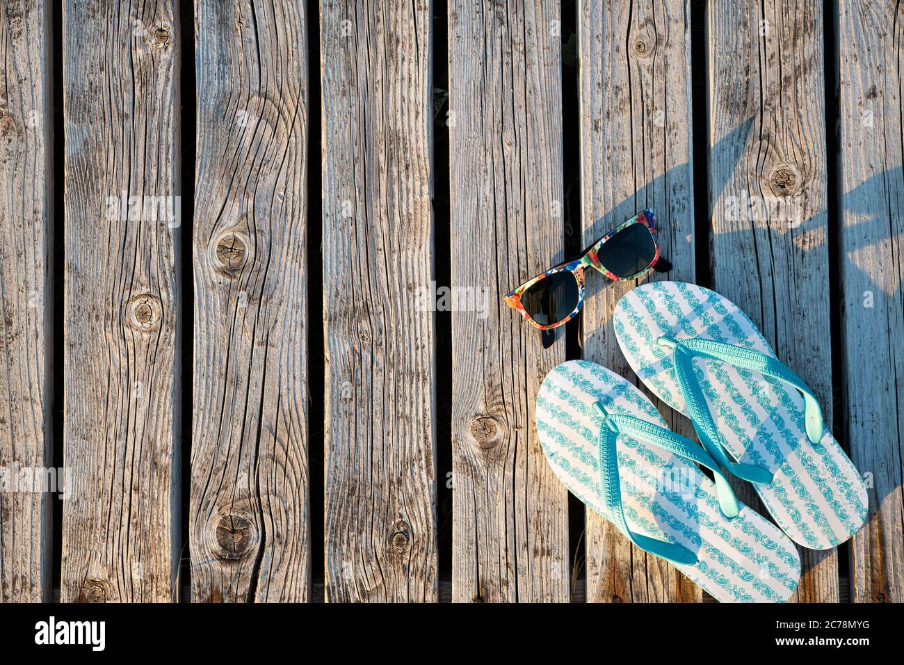Hellblaue Flip Flops und bunte Sonnenbrillen auf einer Holzfläche für einen Hintergrund Stockfoto
