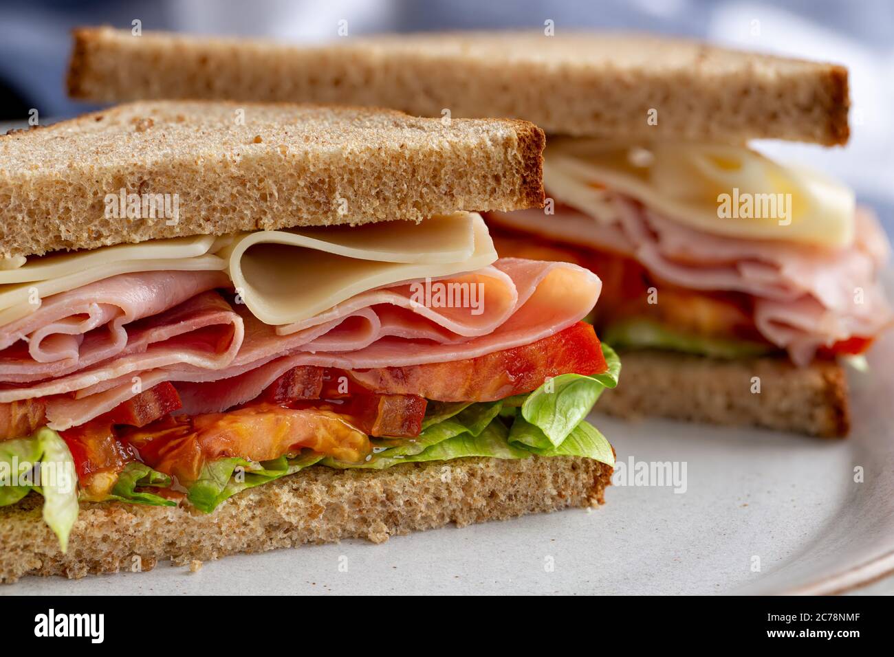 Sandwich mit Schinken, Käse, Salat und Tomaten auf Vollkornbrot, das auf einem Teller halbiert ist Stockfoto