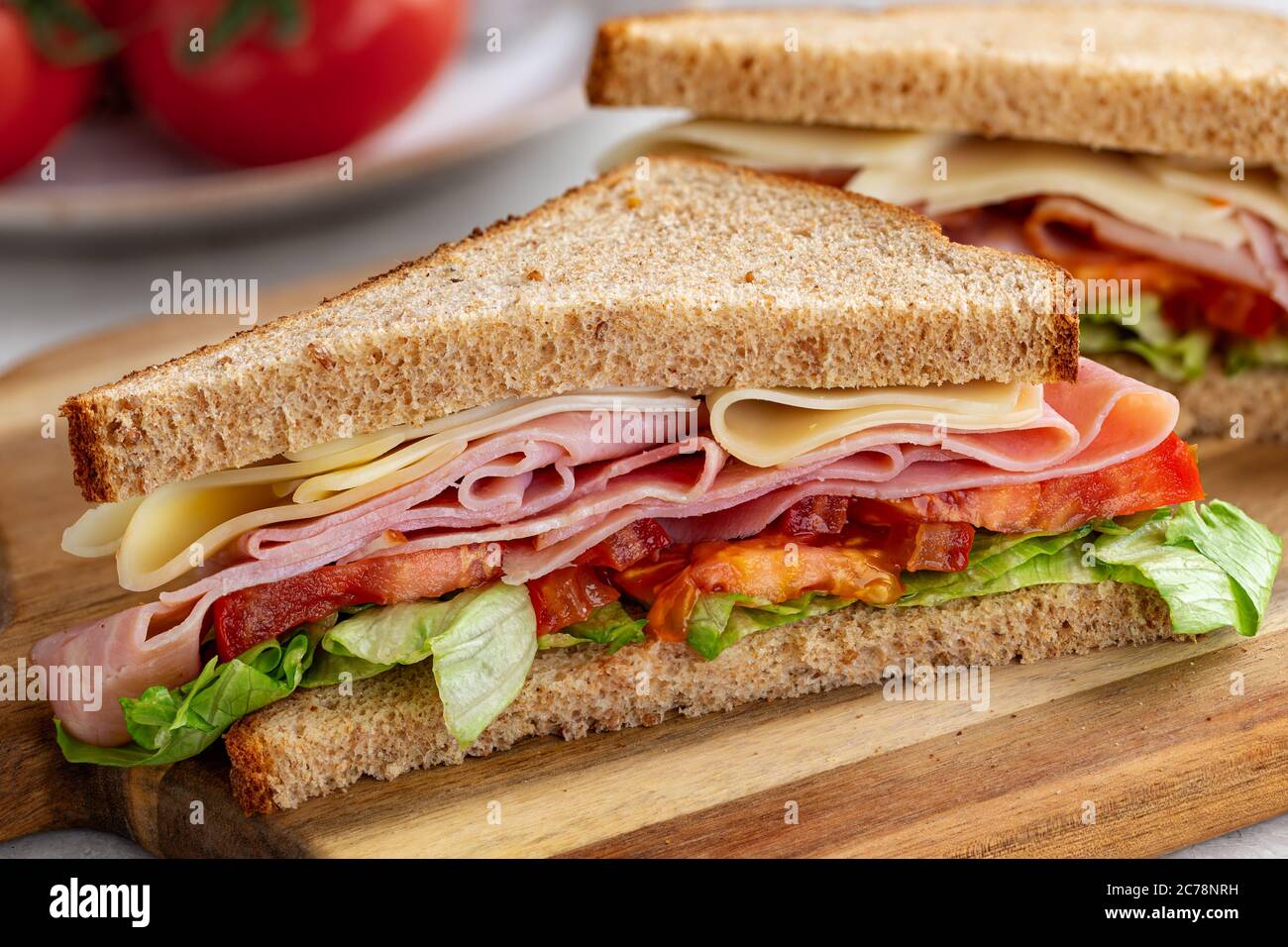 Sandwich mit Schinken, Käse, Salat und Tomaten auf Vollkornbrot, das auf einem Holzbrett halbiert ist Stockfoto