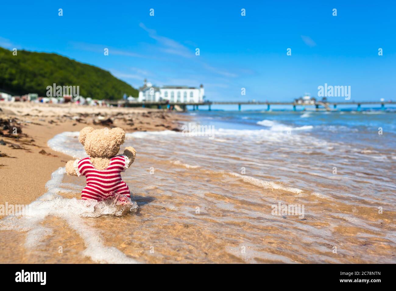 Teddybär im gestreiften nostalgischen Badeanzug Strandleben am Meer in der Nähe des Pier-Gebäudes genießen (Kopierraum) Stockfoto