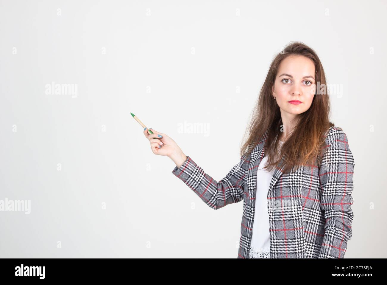 Schöne junge Frau in Business formelle Kleidung posiert gegen eine weiße Wand und zeigt auf etwas Stockfoto