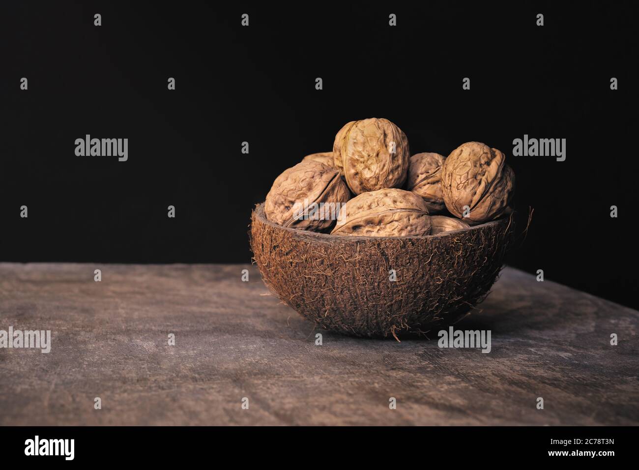 Gruppe von geschälten Walnüssen in einer Kokosnussschale Schale auf einem Holztisch auf schwarzem Hintergrund. Gesunde Ernährung. Stockfoto