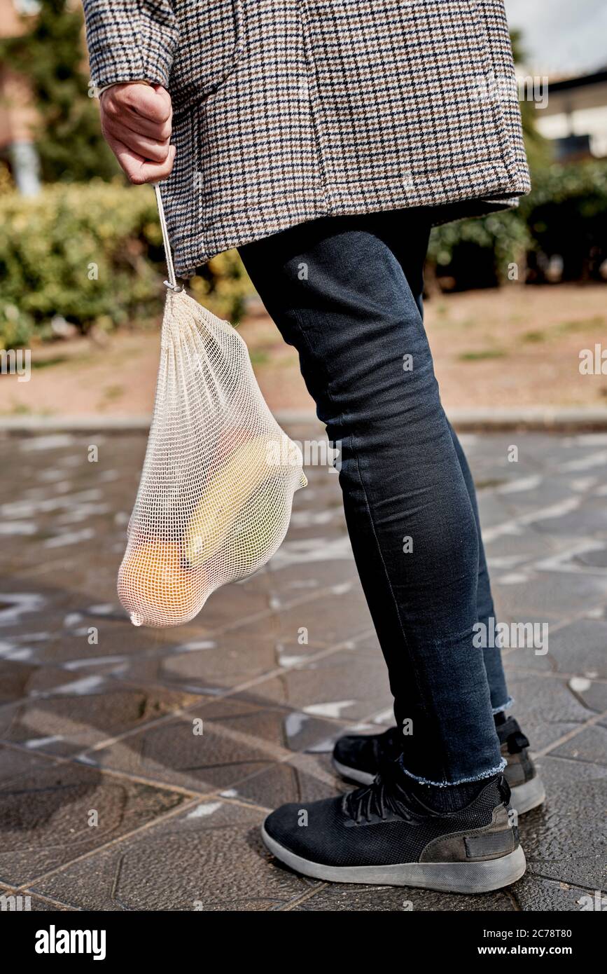 Nahaufnahme eines Mannes auf der Straße, von hinten gesehen, mit einem wiederverwendbaren Netzbeutel aus Textil, der früher Lebensmittel in großen Mengen, voller Obst und Gemüse, kaufte, A. Stockfoto