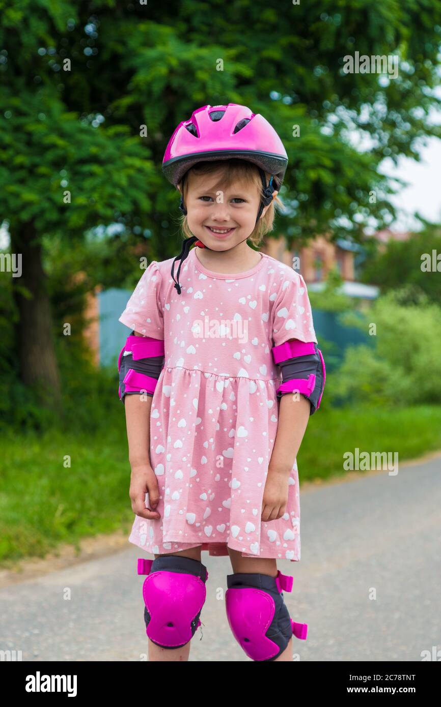 Ein kleines Mädchen rollt in voller Schutz auf einer Dorfstraße. Das Konzept eines aktiven gesunden Lebensstils und sicheren Fahrens. Stockfoto