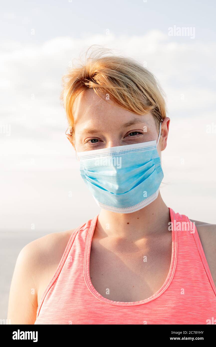 Vertikales Porträt einer schönen blonden Frau mit einer Schutzmaske mit dem Himmel im Hintergrund, Konzept der Prävention und Gesundheitsversorgung Stockfoto