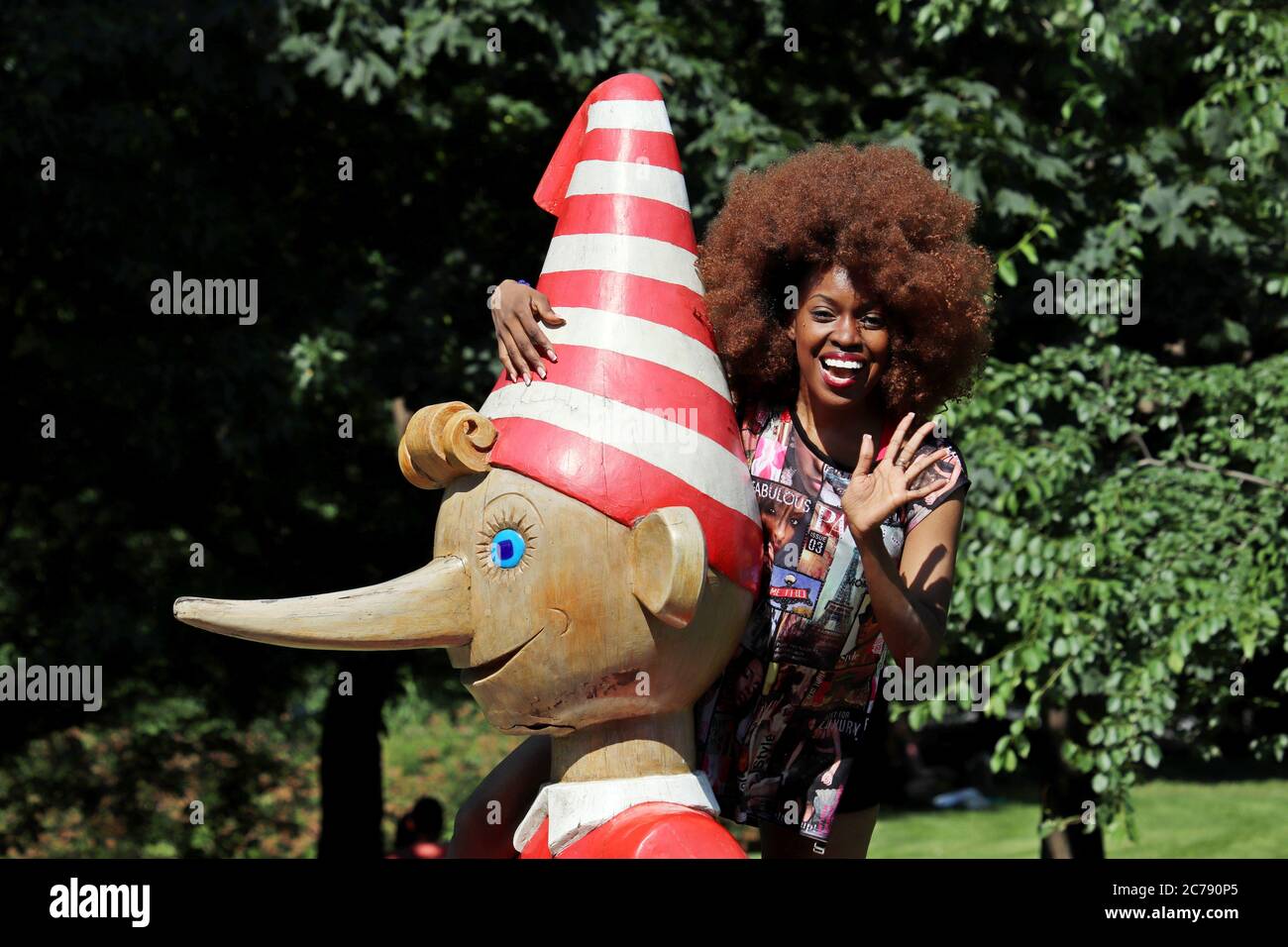 Glückliche schwarze Frau umarmt eine hölzerne Statue von Pinocchio im Muzeon Park im Sommer. Tourist in Russland, russische Sehenswürdigkeiten Stockfoto