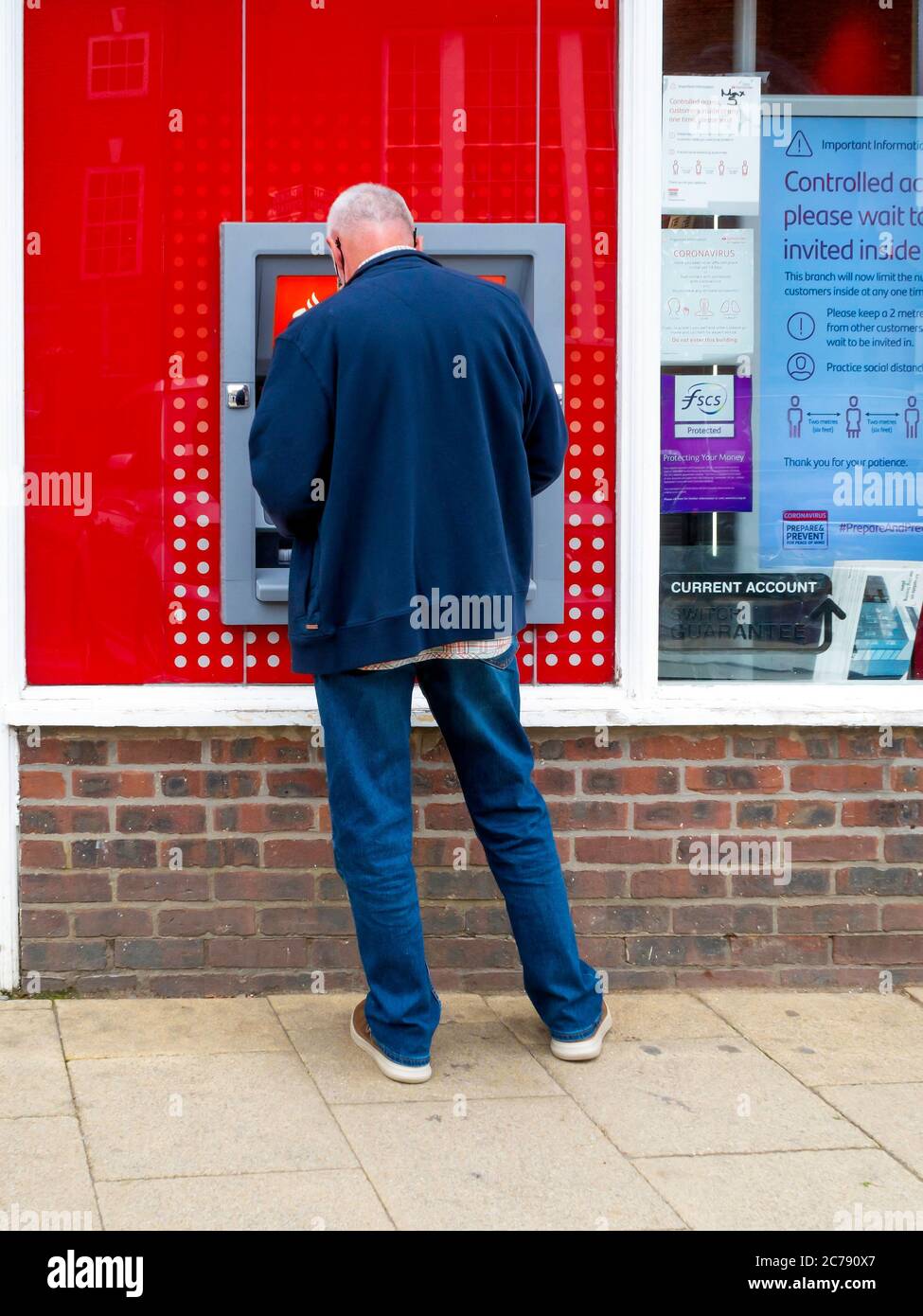 Ein lässig gekleideter älterer Mann, der einen Geldautomaten von Santander benutzt Stockfoto