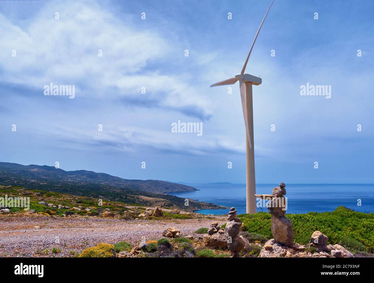 Eine Windmühle Turbine, Straße und balancierende Steine auf dem Hügel der Küste in bunten Landschaft bei dynamischen blauen Himmel an klaren sonnigen Sommertag. Stockfoto
