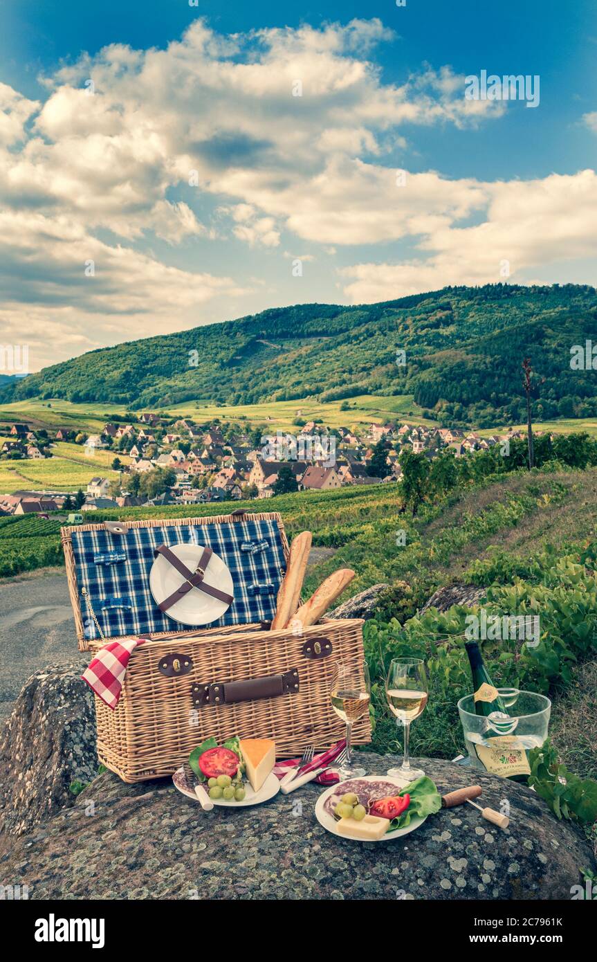 Retro Vintage französischer Picknickkorb mit Käsebrot und Gewürztraminer Wein in den Weinbergen oberhalb des mittelalterlichen Dorfes Riquewihr Elsass Frankreich Stockfoto