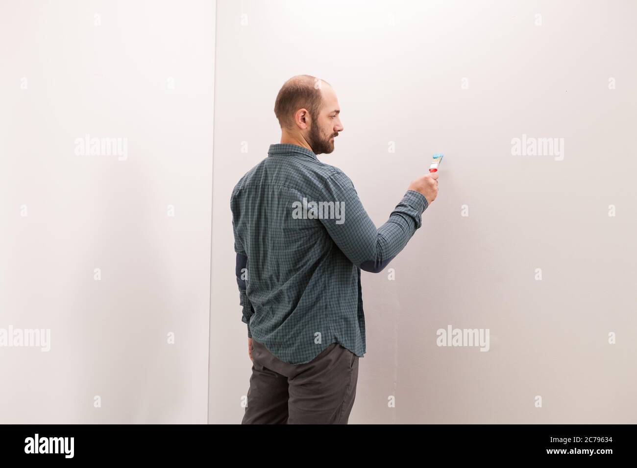 Ehemann testet die Farbe an der Wand mit einem kleinen Pinsel. Haus während der Renovierung, Dekoration und Malerei. Innenwohnung Verbesserung Wartung. Roller, Leiter für Hausreparatur Stockfoto