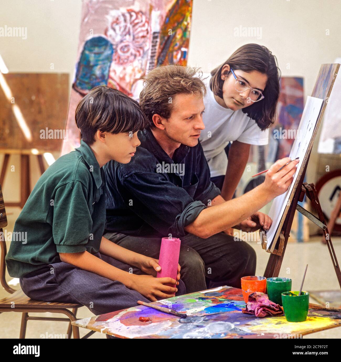 KUNSTKLASSE Junior School Lehrer und Junior Mädchen & Jungen Schüler arbeiten an einem Aquarell Malerei in einer Schule Kunst Klassenzimmer Stockfoto