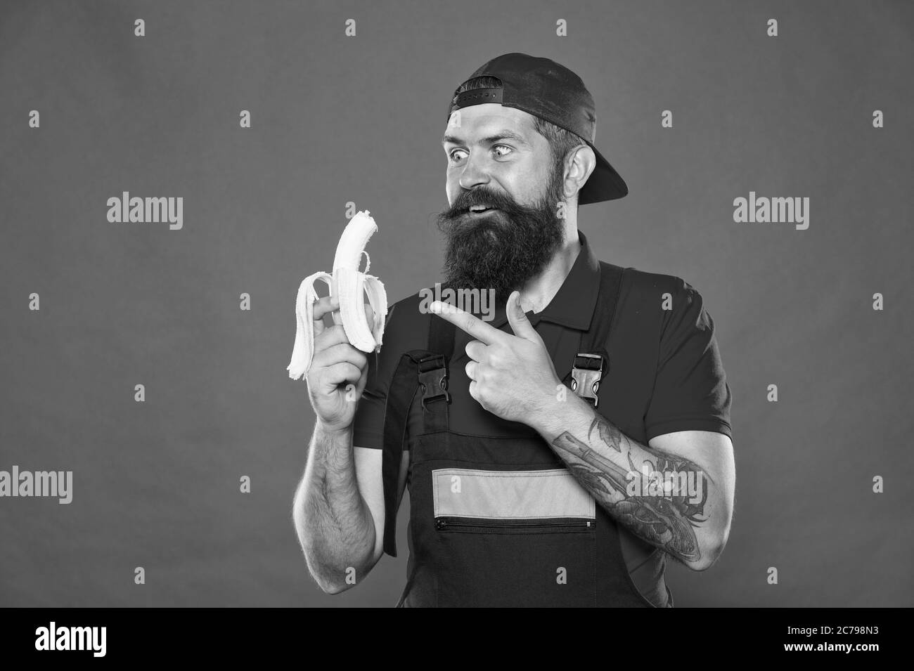 Hungriger Flusspferd. Frisches Obst. Gesundes Leben. Leckeres Essen. Bissen Sie Banane. Bevorzugter Snack. Lebensmittelgericht. Mittagszeit. Bärtiger Mann in Uniform und Kappe, der Banane isst. Arbeiter Erbauer Mechaniker essen Banane. Stockfoto