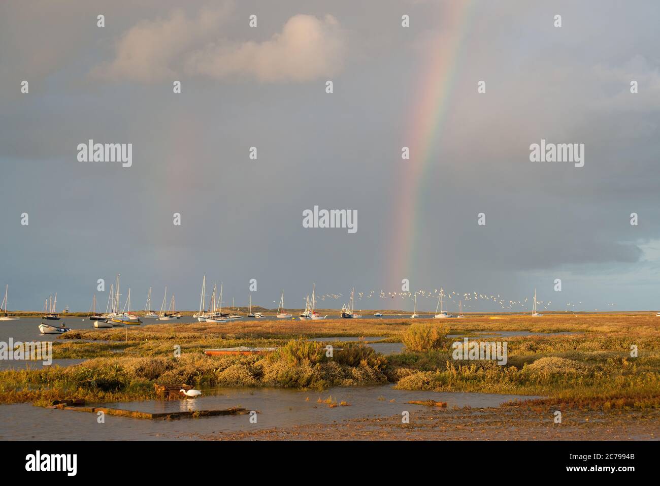 Am frühen Abend bei Brancaster Staithes mit einem doppelten Regenbogen und meisterten Segelbooten vor Anker im klassischen Abendlicht Stockfoto