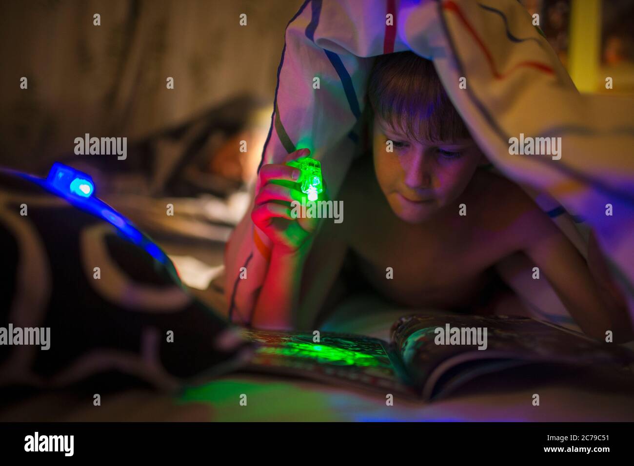 Junge mit grüner Taschenlampe Lesemagazin unter Decke Stockfoto