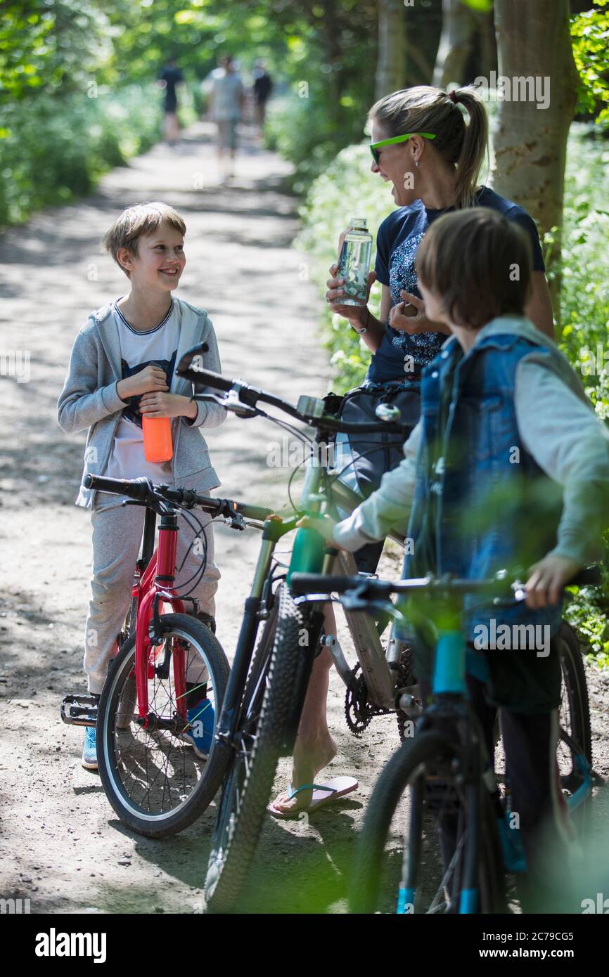 Mutter und Söhne trinken Wasser auf Radtour im sonnigen Park Stockfoto