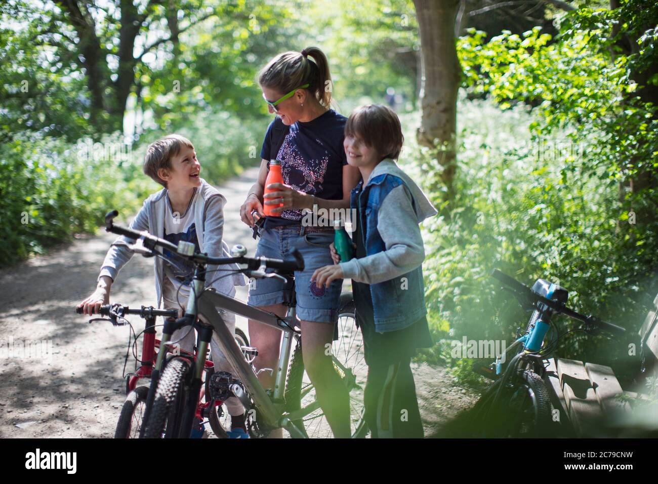 Mutter und Söhne trinken Wasser auf Radtour im sonnigen Park Stockfoto