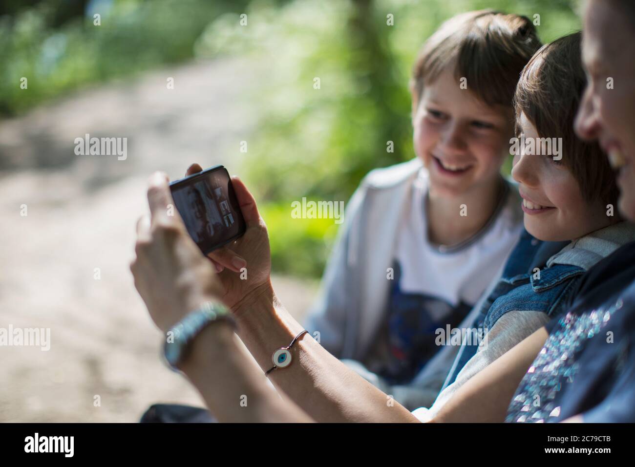 Mutter und Söhne Video chatten mit Freunden auf Smartphone im Park Stockfoto