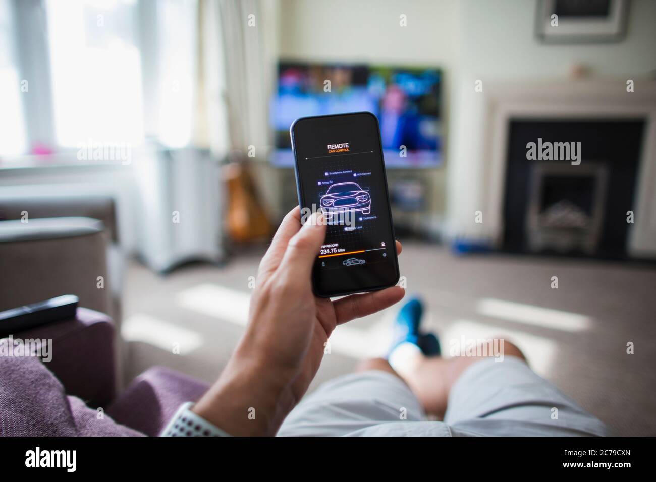 POV man überprüft die Fernbedienung des Autos auf dem Smartphone im Wohnzimmer Stockfoto
