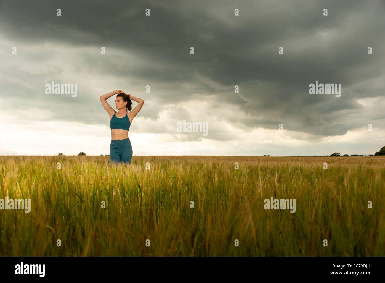 Sportliche Frau bindet ihre Haare zurück vor dem Training, dramatische Himmel und Landschaft. Stockfoto