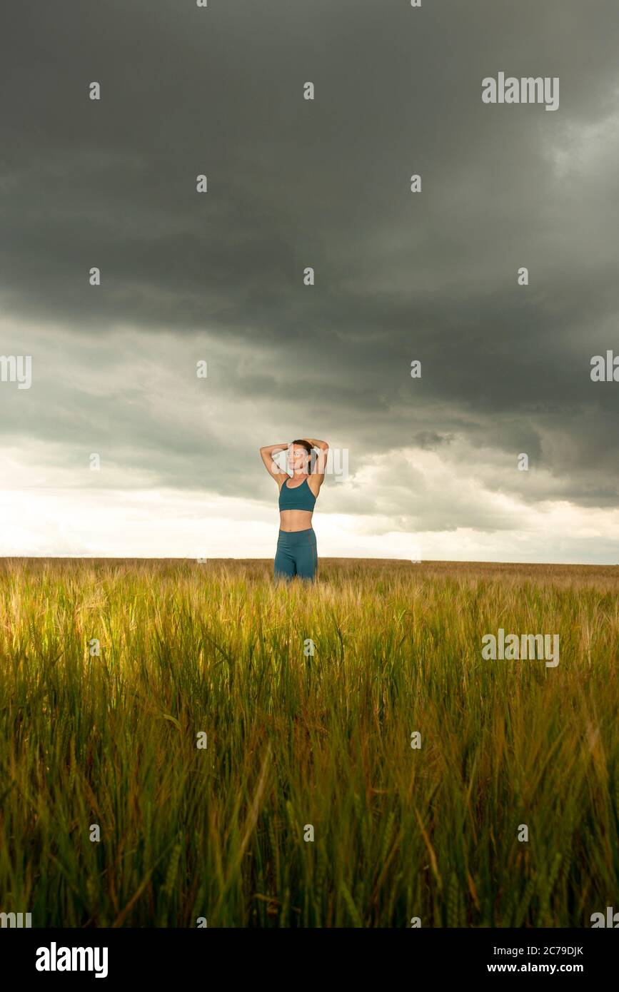 Sportliche Frau, die sich nach dem Training in der Mitte eines Weizenfeldes mit dramatischem Himmel ausruhen Stockfoto