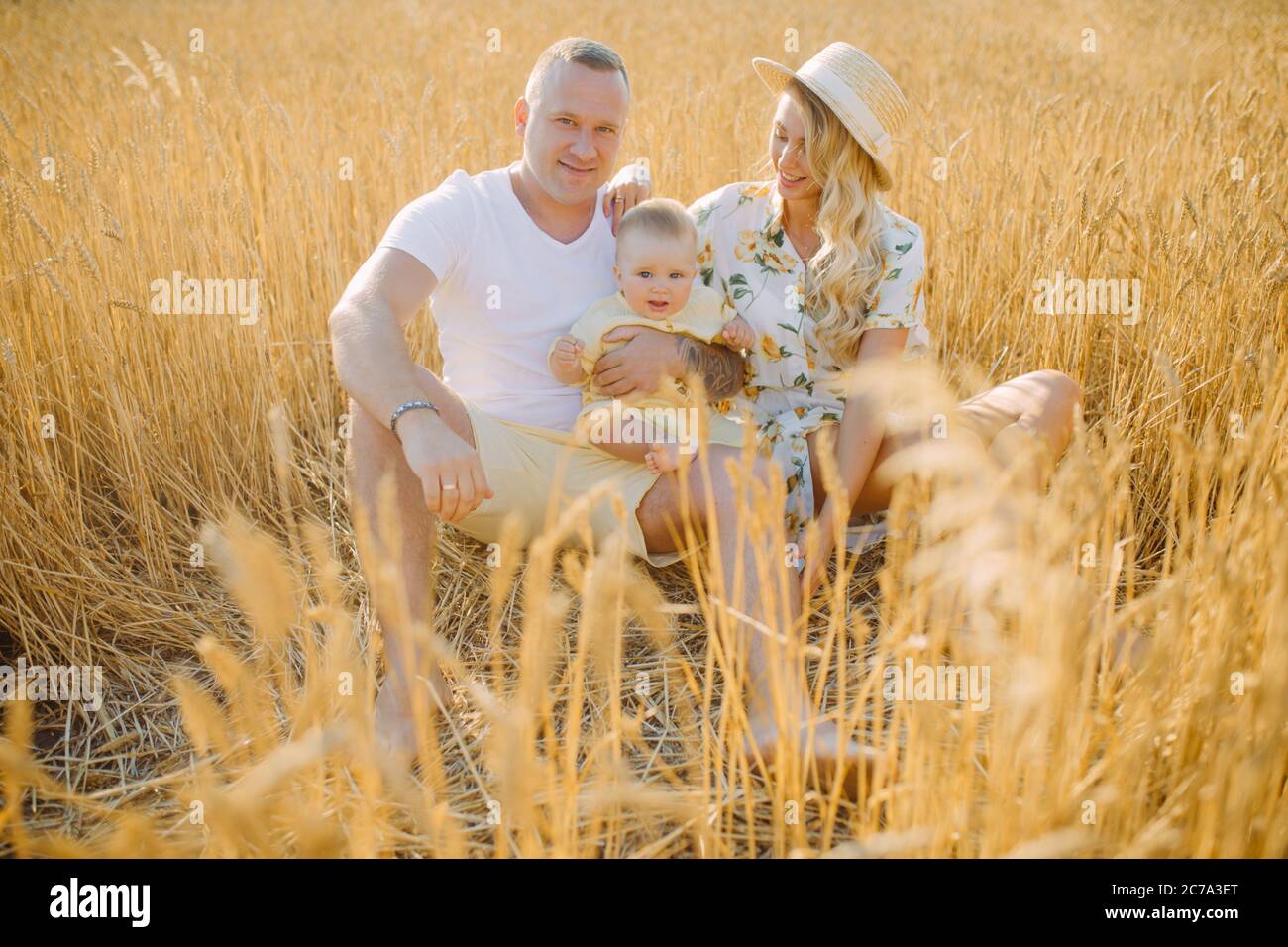 Glückliche junge Familie mit Baby ruht zwischen gelben Weizenfeld. Stockfoto