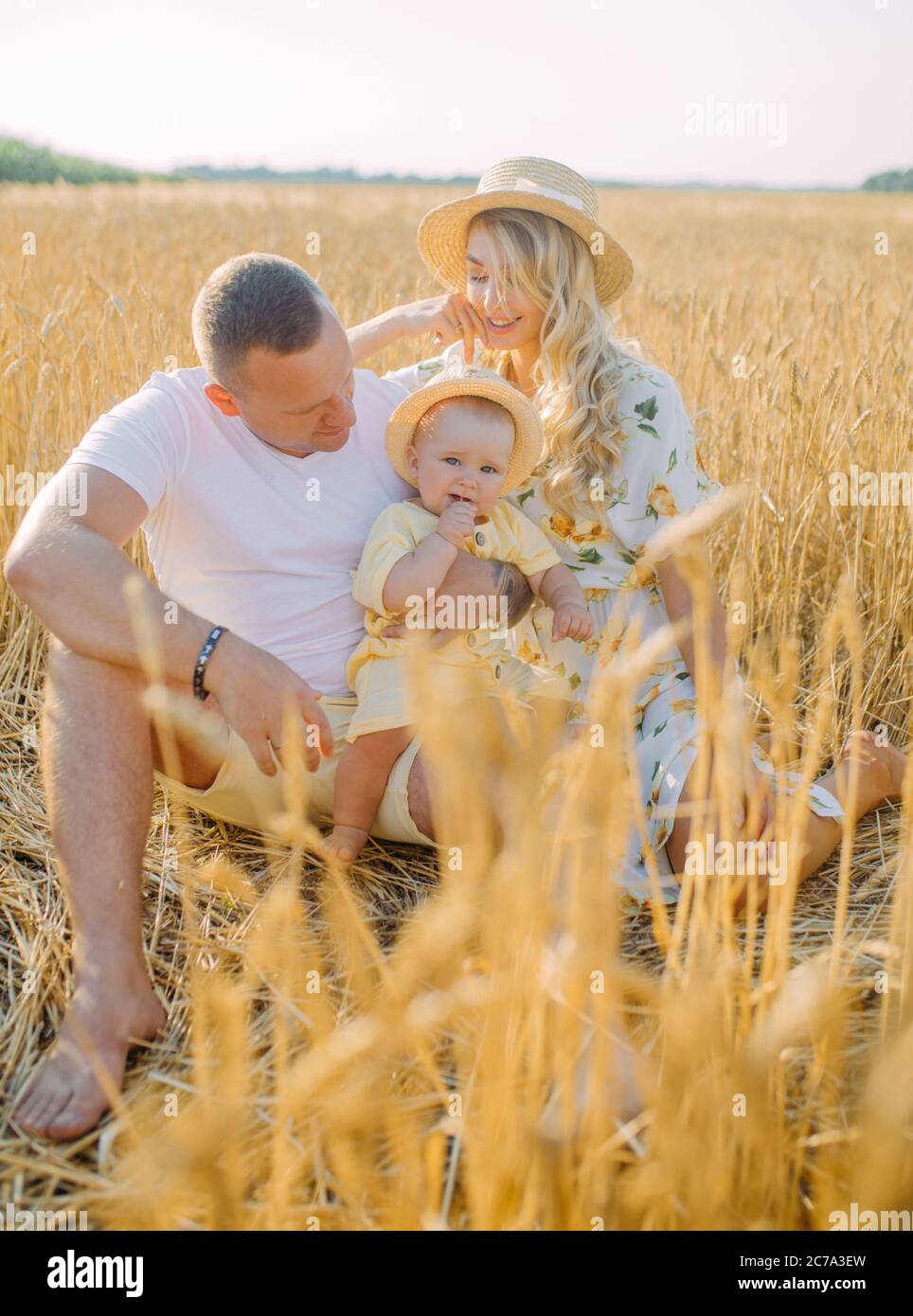 Glückliche junge Familie mit Baby sitzt und ruht zwischen gelben Weizenfeld. Stockfoto