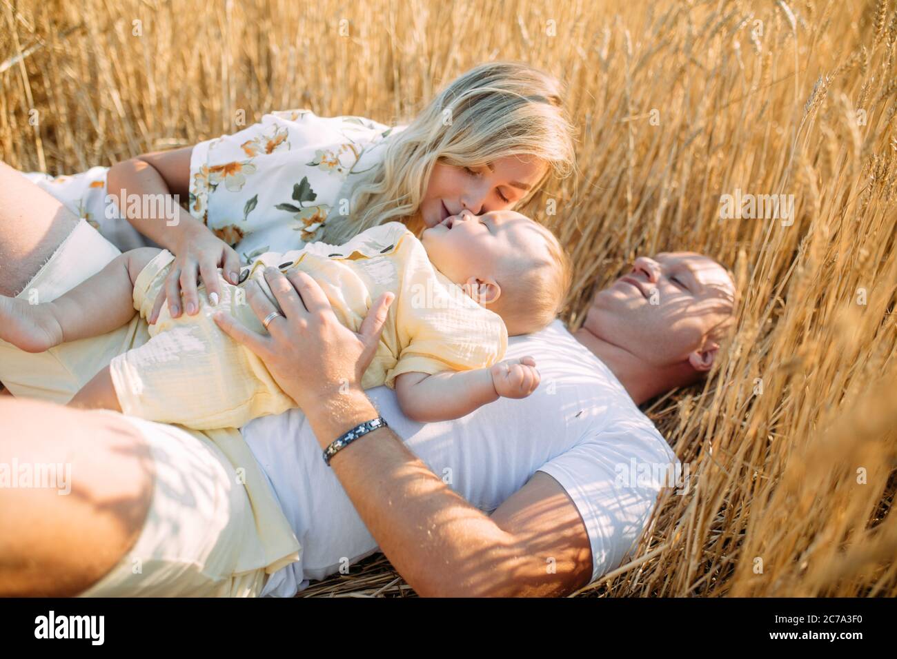 Glückliche junge Familie mit Baby liegen und Ruhe zwischen gelben Weizenfeld. Nahaufnahme. Stockfoto
