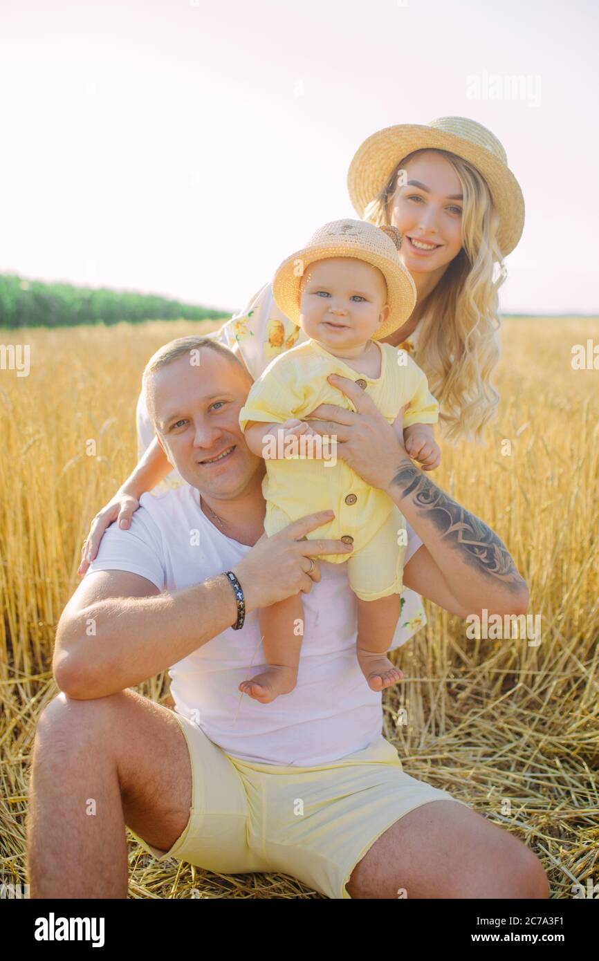 Glückliche junge Familie mit Baby sitzt und ruht zwischen gelben Weizenfeld. Stockfoto