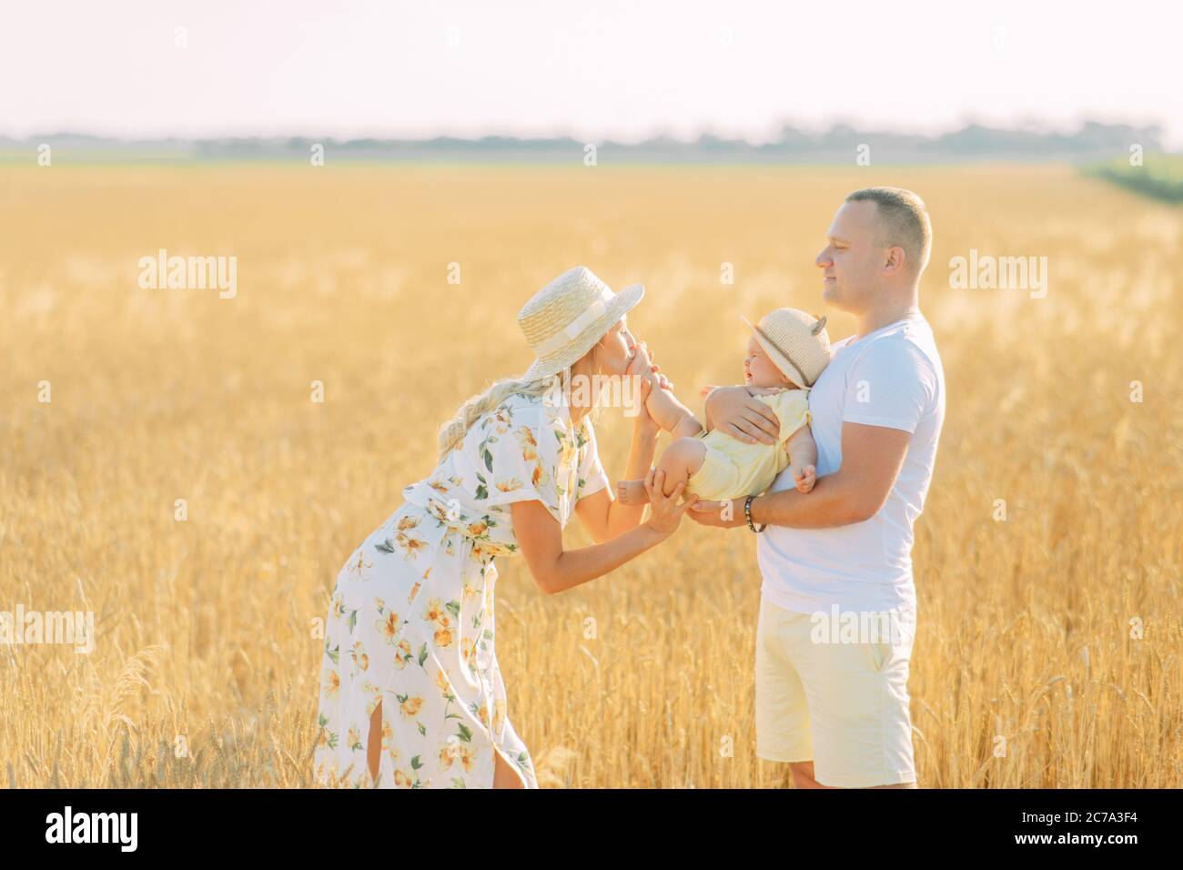 Glückliche junge Familie hat Spaß und spielt mit ihrem Baby unter gelben Weizenfeld. Stockfoto
