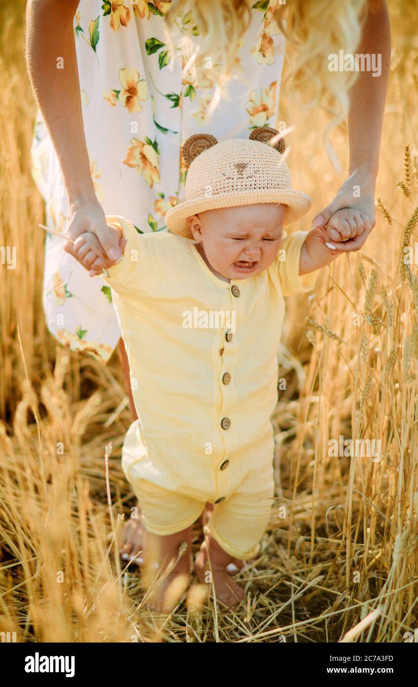 Mutter führt und hält ihr weinendes Baby mit den Händen im gelben Weizenfeld. Stockfoto
