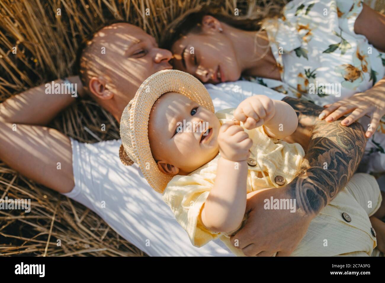 Glückliche junge Familie mit Baby liegen und Ruhe zwischen gelben Weizenfeld. Nahaufnahme. Stockfoto