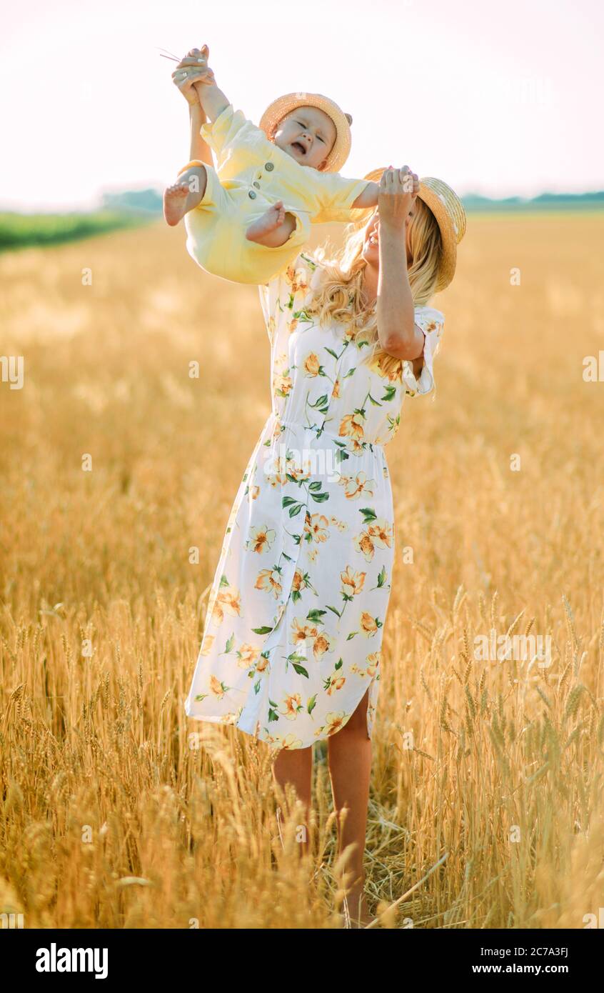 Glückliche junge Mutter hat Spaß und spielt mit ihrem Baby zwischen gelben Weizenfeld. Stockfoto
