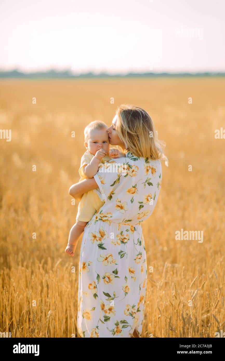 Glückliche junge Mutter geht mit ihrem Baby zwischen gelbem Weizenfeld. Stockfoto