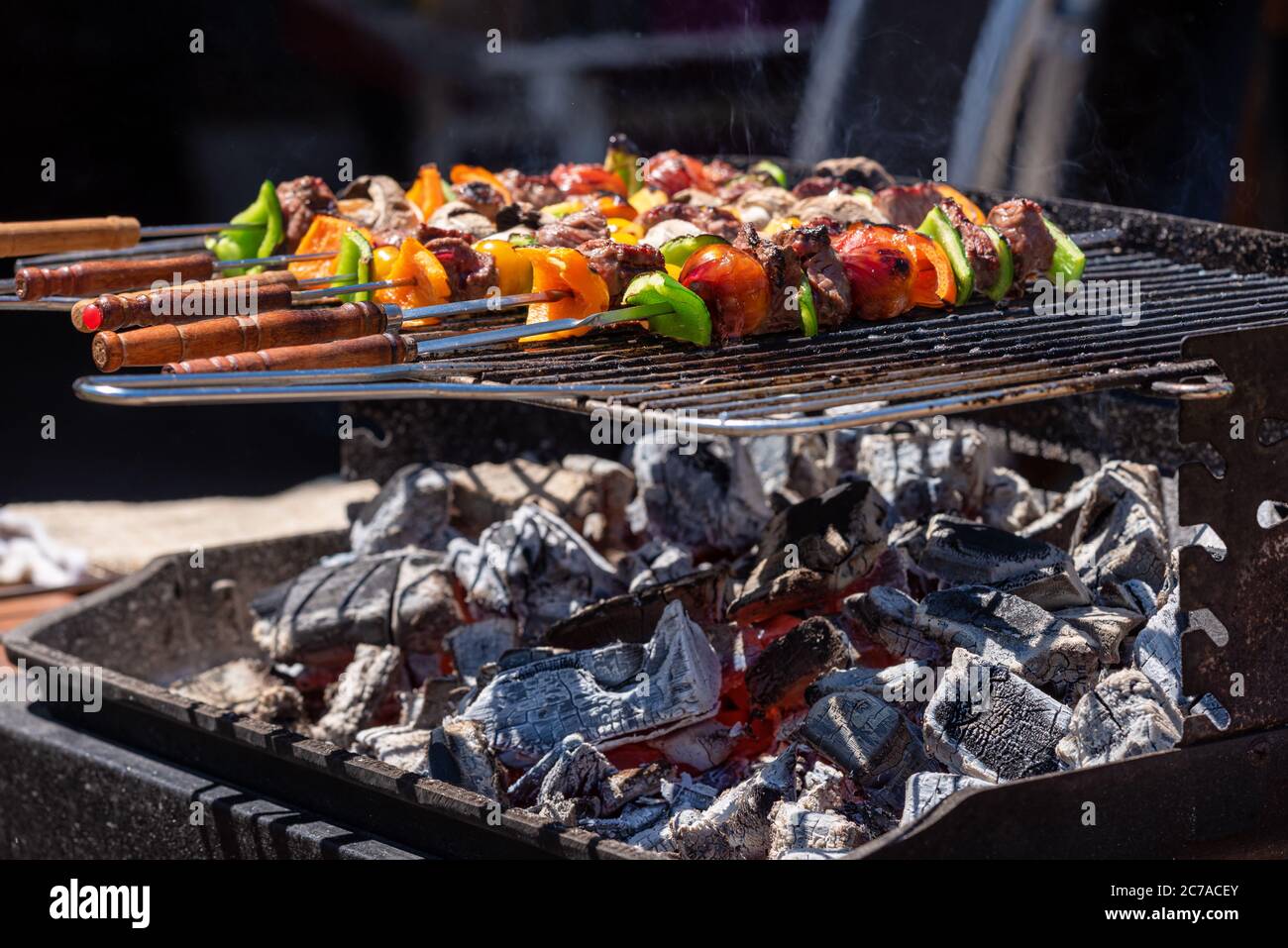 Gegrillte Grillspieße von Gemüse und Fleisch auf dem Grill im Freien. Leuchtende Kohle sichtbar. Stockfoto