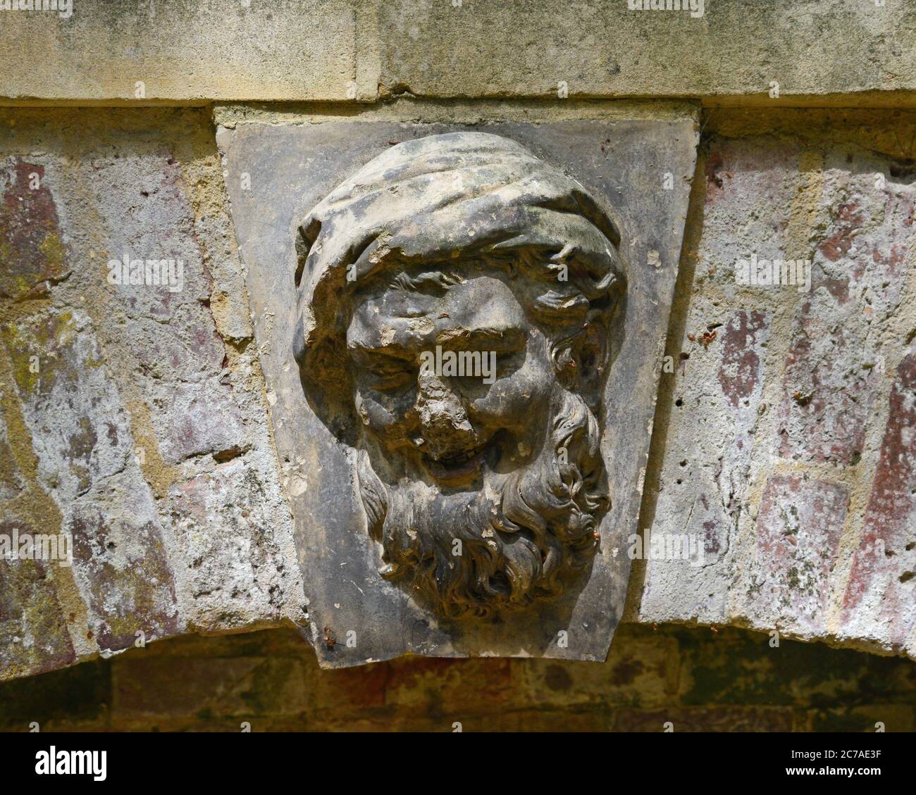 Dieses lächelnde Steingesicht befindet sich in der Mitte eines niedrigen Ziegelbogens versteckt in einer Ecke des Dutch Garden, Bridge End Garden, Saffron Walden, Essex. Zoll Stockfoto
