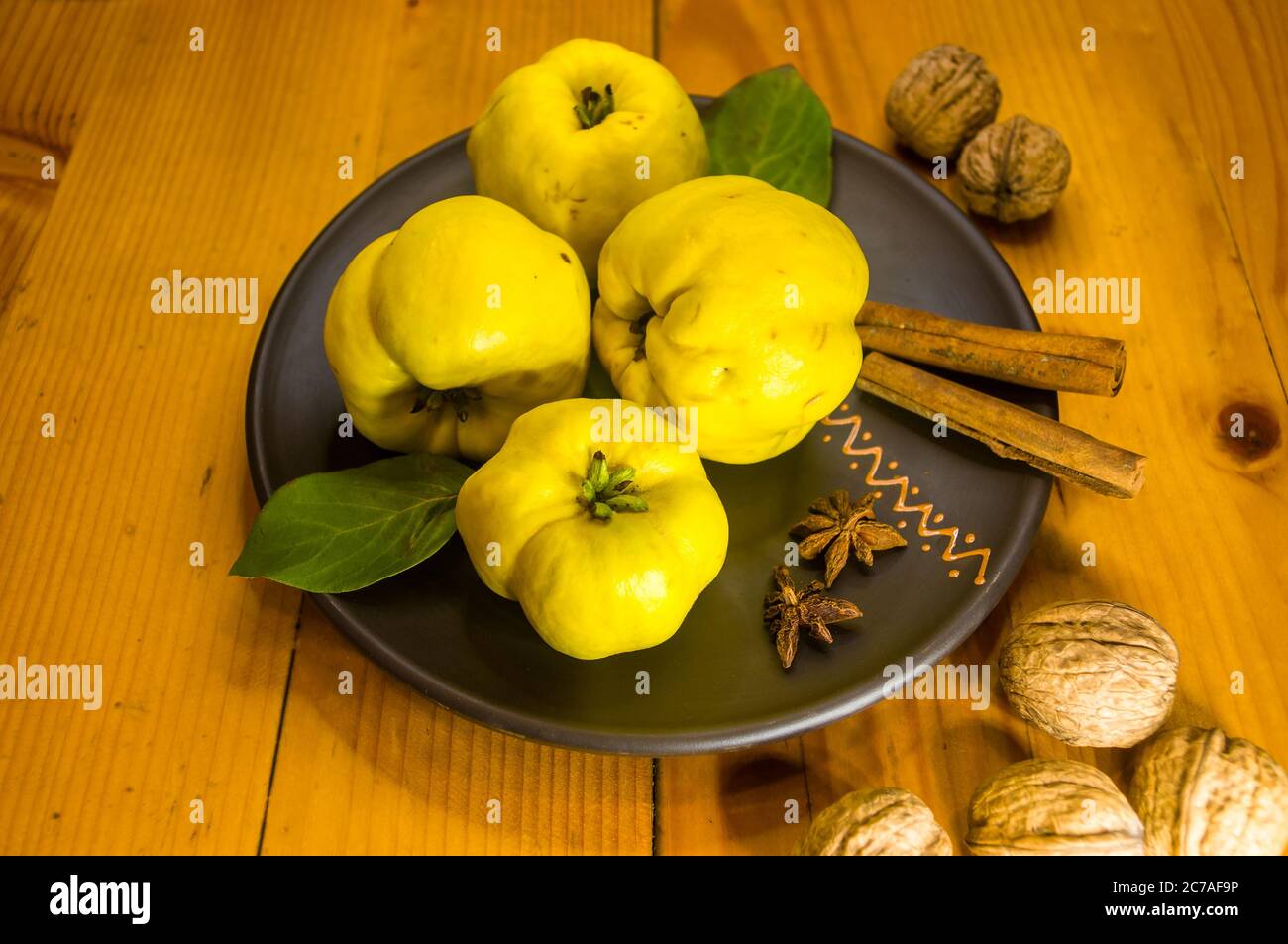 Große gelbe Quinzfrüchte auf einer Keramikplatte mit Anis, Zimt und Walnüssen Stockfoto
