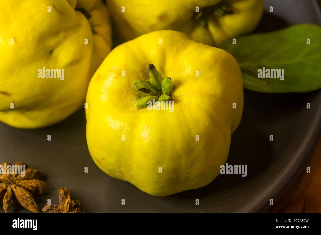 Große gelbe Quinzfrüchte auf einer Keramikplatte mit Anis, Zimt und Walnüssen Stockfoto