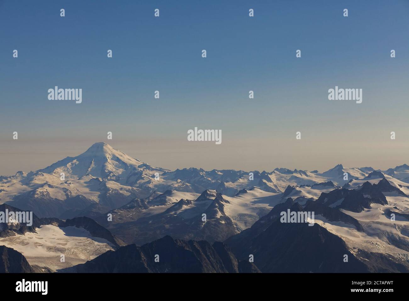 Schneebedeckter vulkanischer Berg mit einer Rauchwolke, die über den Himmel strömt und die dramatische und zerklüftete Wildnis Alaskas zeigt. Stockfoto