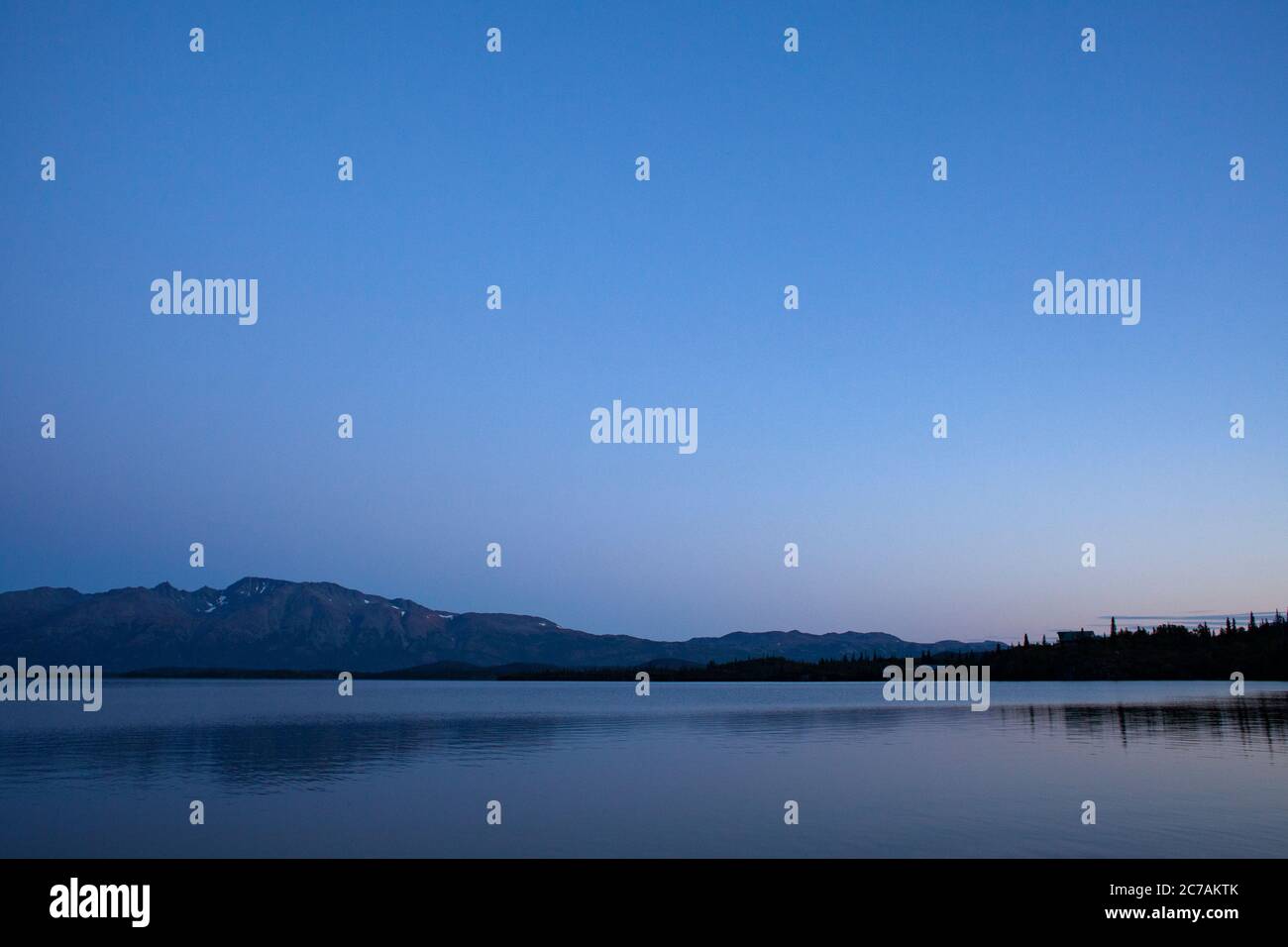 Ruhige Dämmerung über dem Lake Iliamna, Alaska, mit ruhigem Wasser, das die sanften Töne des Abendhimmels und die Silhouetten der Berge reflektiert. Stockfoto