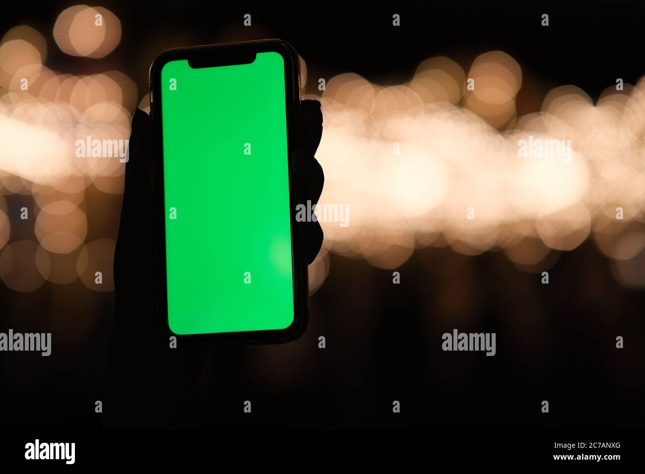 Nahaufnahme mit einer Hand und Smartphone mit grünem Bildschirm in der Nacht. Schöne goldene Bokeh Hintergrund Stockfoto
