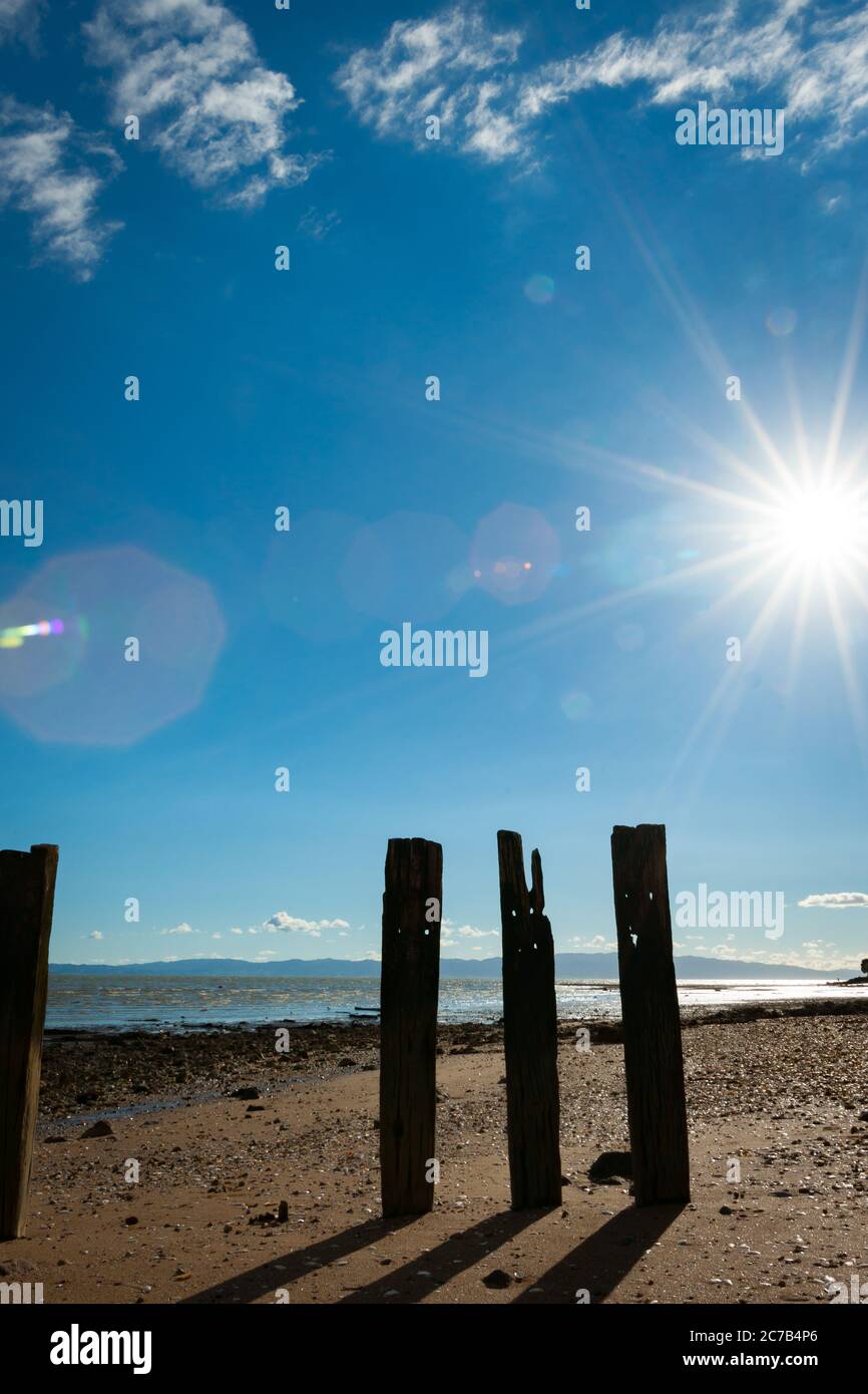 Alte Piers in Silhouette werfen Schatten auf Sand bei Ebbe mit Linse Flare von Starburst Sonne. Stockfoto