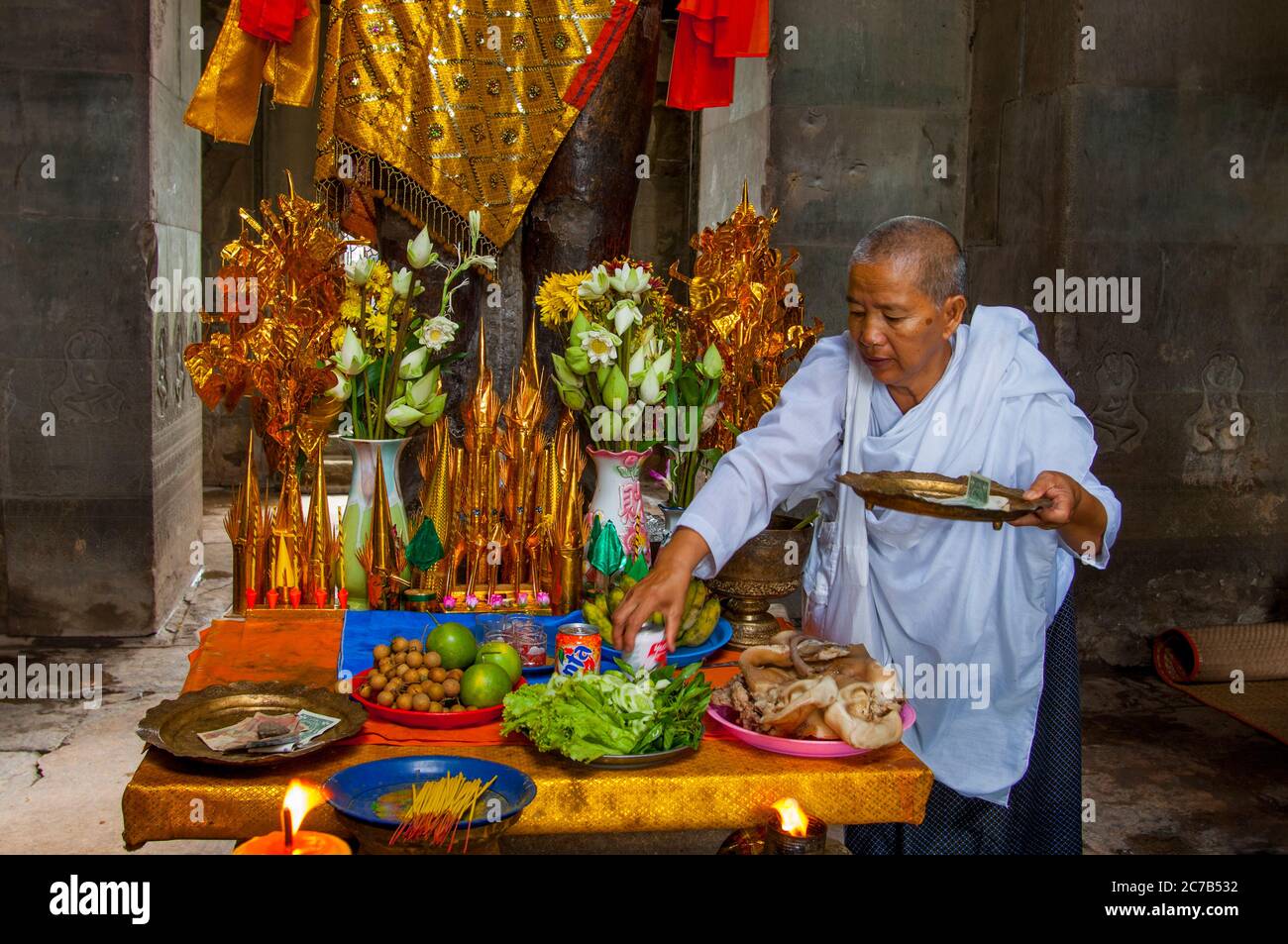 Eine buddhistische Nonne ordnet Opfergaben an der Basis einer dekorierten Statue von Herrn Vishnu, einem Hindu-gott, dem Obersten Gott des Vaishnavismus (einer der drei Stockfoto